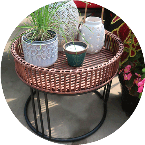 A brown wicker type plant stand with black metal legs, holding two lanterns and a potted plant.